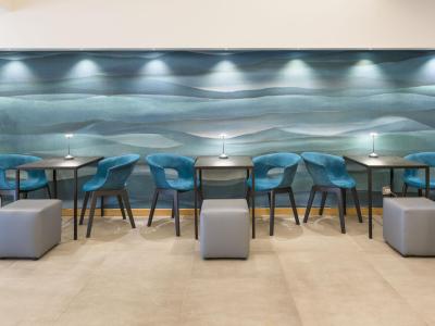 Sala moderna con sedie blu, tavoli neri e parete artistica ondulata.