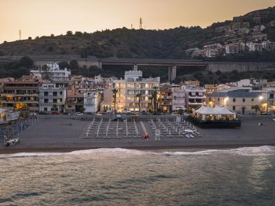 Tramonto su spiaggia tranquilla, case illuminate e colline serene.