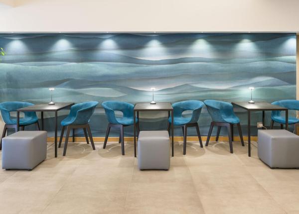 Sala moderna con sedie blu, tavoli neri e parete artistica ondulata.