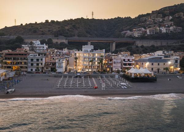 Tramonto su spiaggia tranquilla, case illuminate e colline serene.